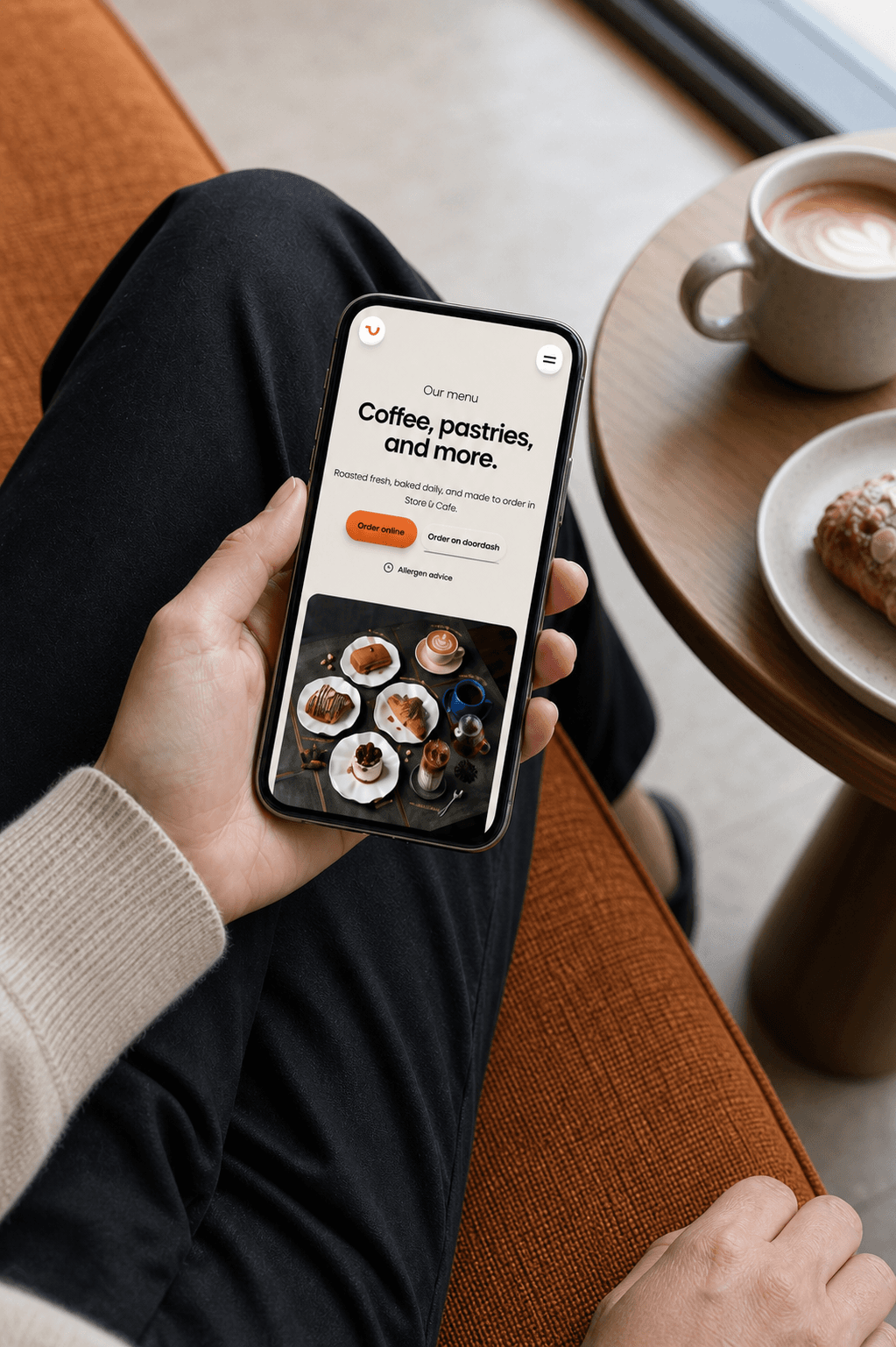 WhatCoffee mobile menu displayed on a phone held beside a cup of coffee and a pastry
